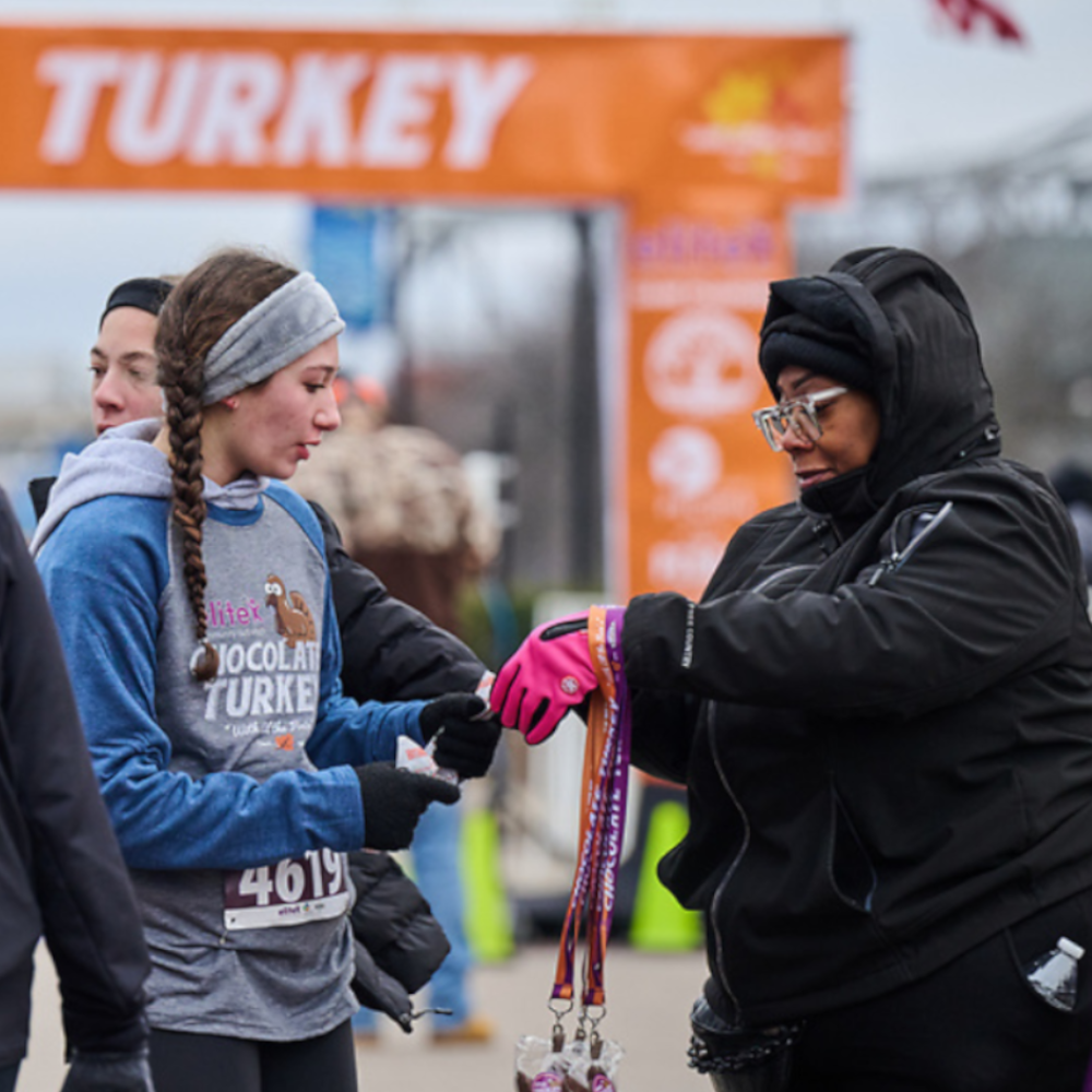 An Elite Community Outreach volunteer hands out a Chocolate Turkey medal to a participant.