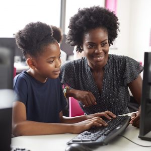 Teacher Helping Female High School Student Working at Screen In Computer Class